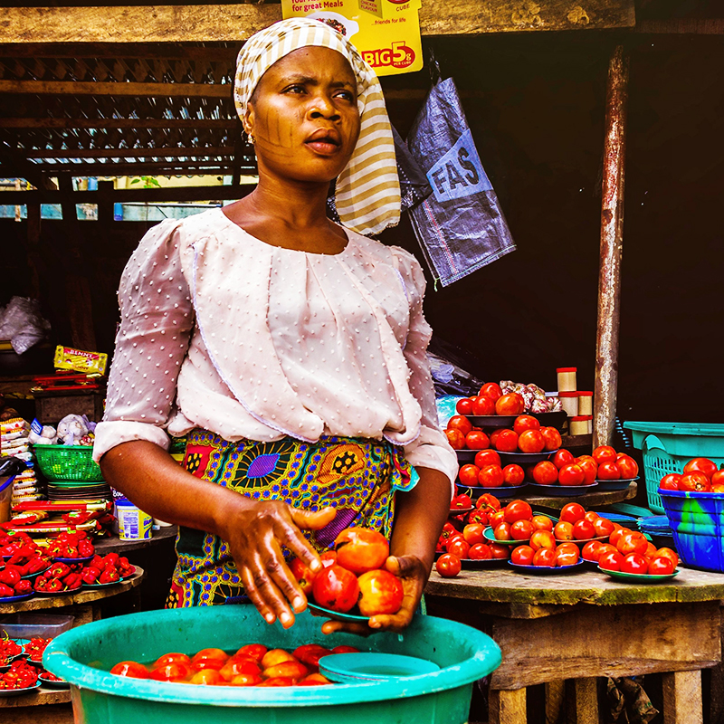 Image of a woman washing tomatoes in front of a bell pepper and tomato stand.