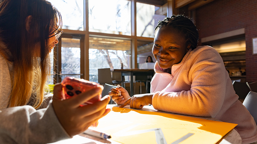 Gelic Jerona ’27 (left) and Benitha Tumukunde ’27 (right) making posters in Reid Campus Center before the 2025 Day of Celebration Legacy Walk in honor of Martin Luther King Jr.