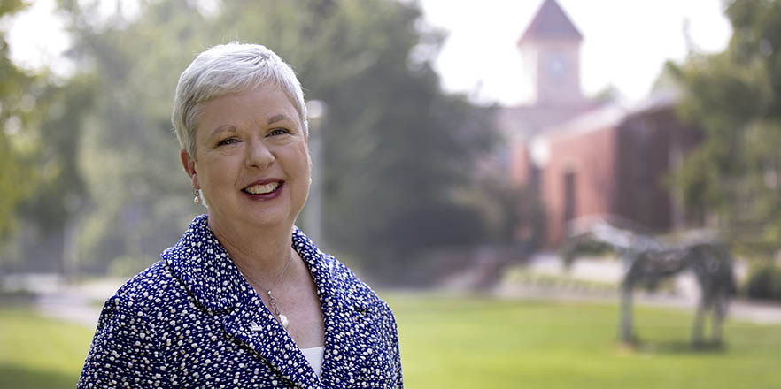 Whitman College President Kathleen Murray stands on campus with the Memorial Building behind her.