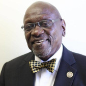 Photograph of a smiling man wearing glasses, a bow tie, and a blazer