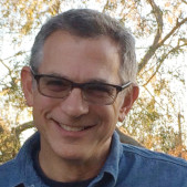 Photograph of a man wearing glasses standing outdoors, smiling to the camera