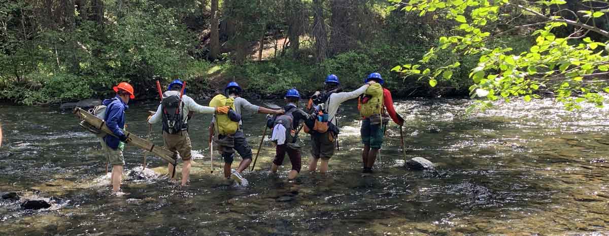 Whitman students crossing a river to performing trail work