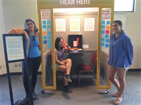 Maddy, Erina, and Donovan pose in front of the "Hear Here" telephone booth.