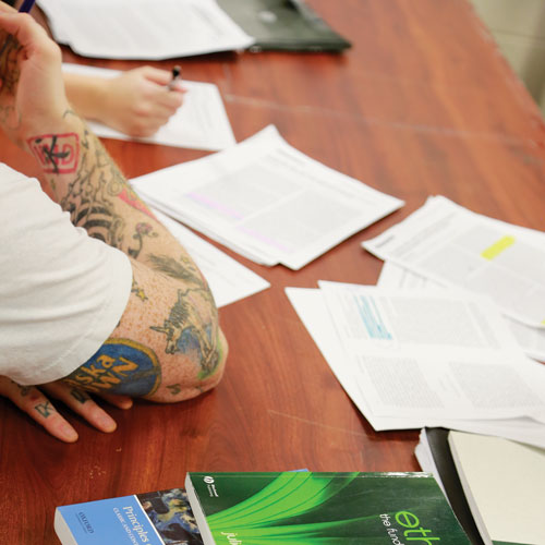 View of tattooed arm resting on desk with books