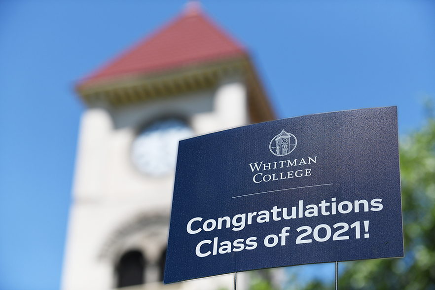 A yard sign reading "Congratulations Class of 2021" is displayed with the clock tower of Memorial Building in the background. 