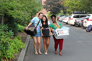 Three students carry luggage into the residence halls during move-in.