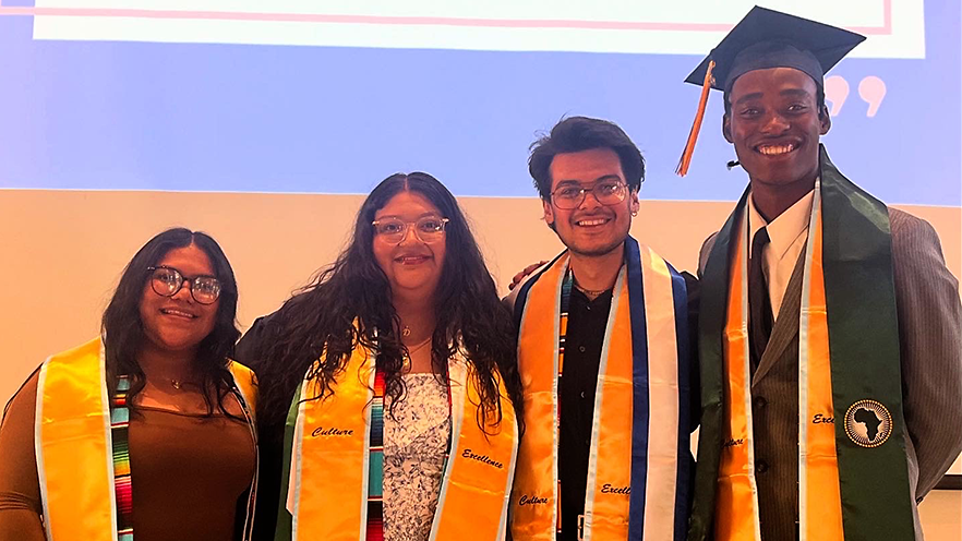 Four students wearing colorful stoles on top of graduation regalia.