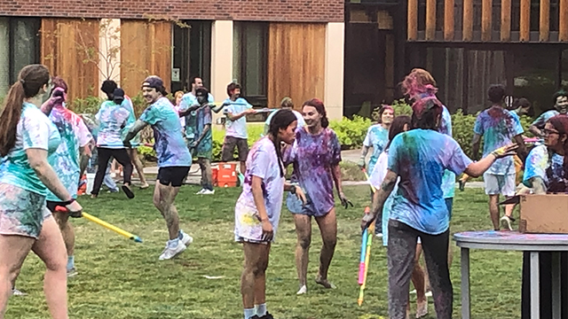 Students celebrating Holi, wearing white shirts covered with multicolored stains.