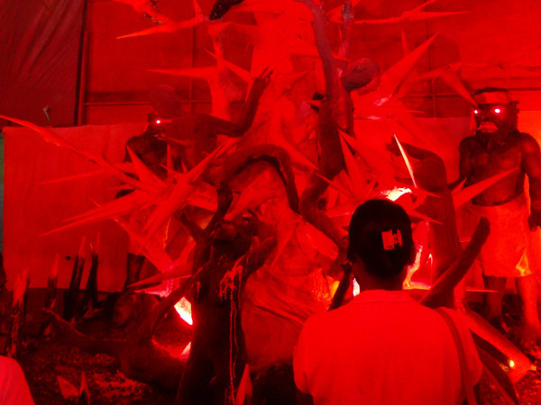 Photograph of a woman looking at a sculpture of a thorny tree, with a body impaled on a branch.