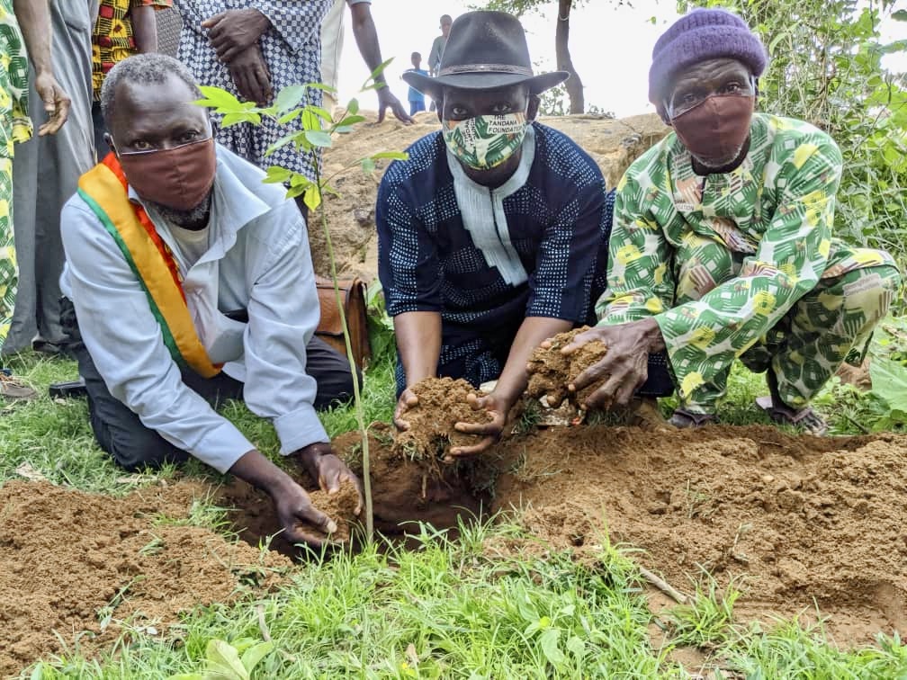 Three men in colorful clothes, kneeling and cupping dirt in their hands