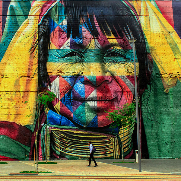 Mural of older individual with a younger individual walking past it while on the phone.