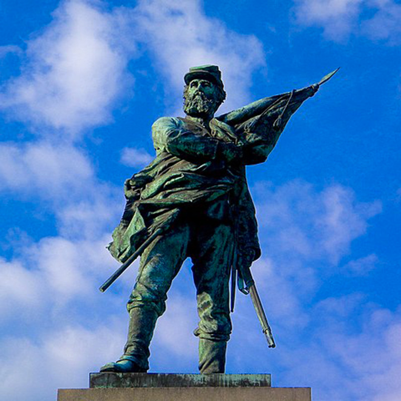 Statue of a confederate soilder holding a flag close to his body.