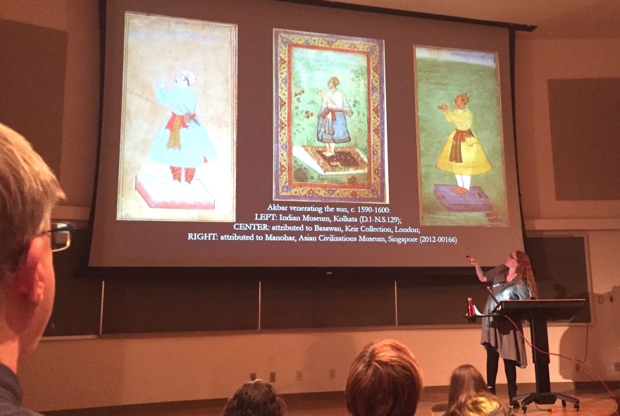 Professor Krista Gulbransen gives a lecture to an auditorium full of people on three portraits presented on a screen.