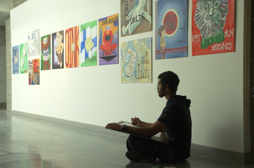 a student sits in the hallway of the art building working on a drawing
