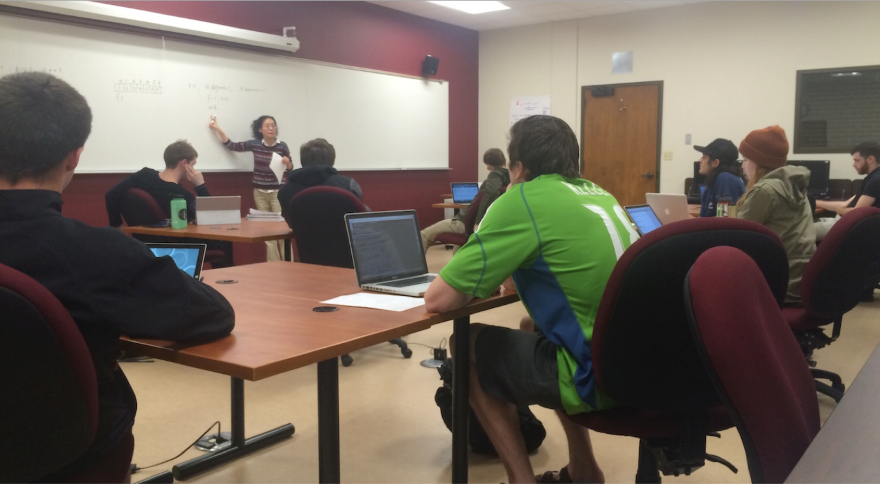 Students sit at desks with laptop computers while receiving instructions 