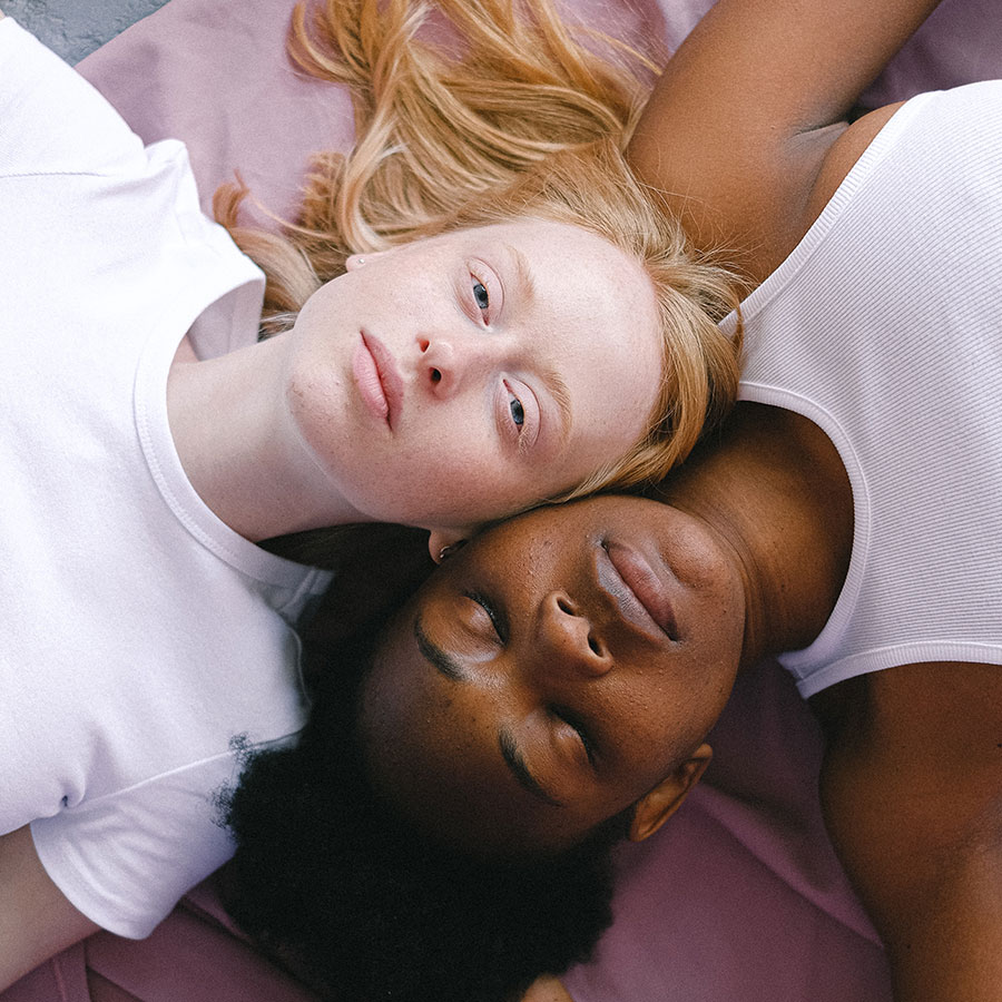 Two persons lying next to each other; one is black and one is white.