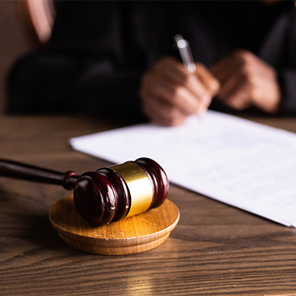 A gavel on a table with someone writing in the background.