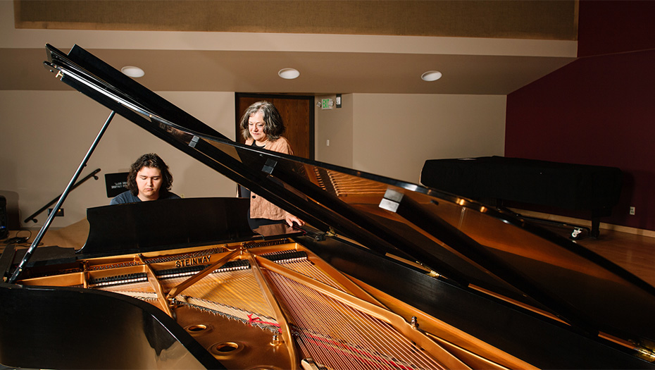 Student playing a piano with their teacher watching.