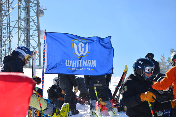 Alpine Skiing team, blue Whitman flag, with snowy background