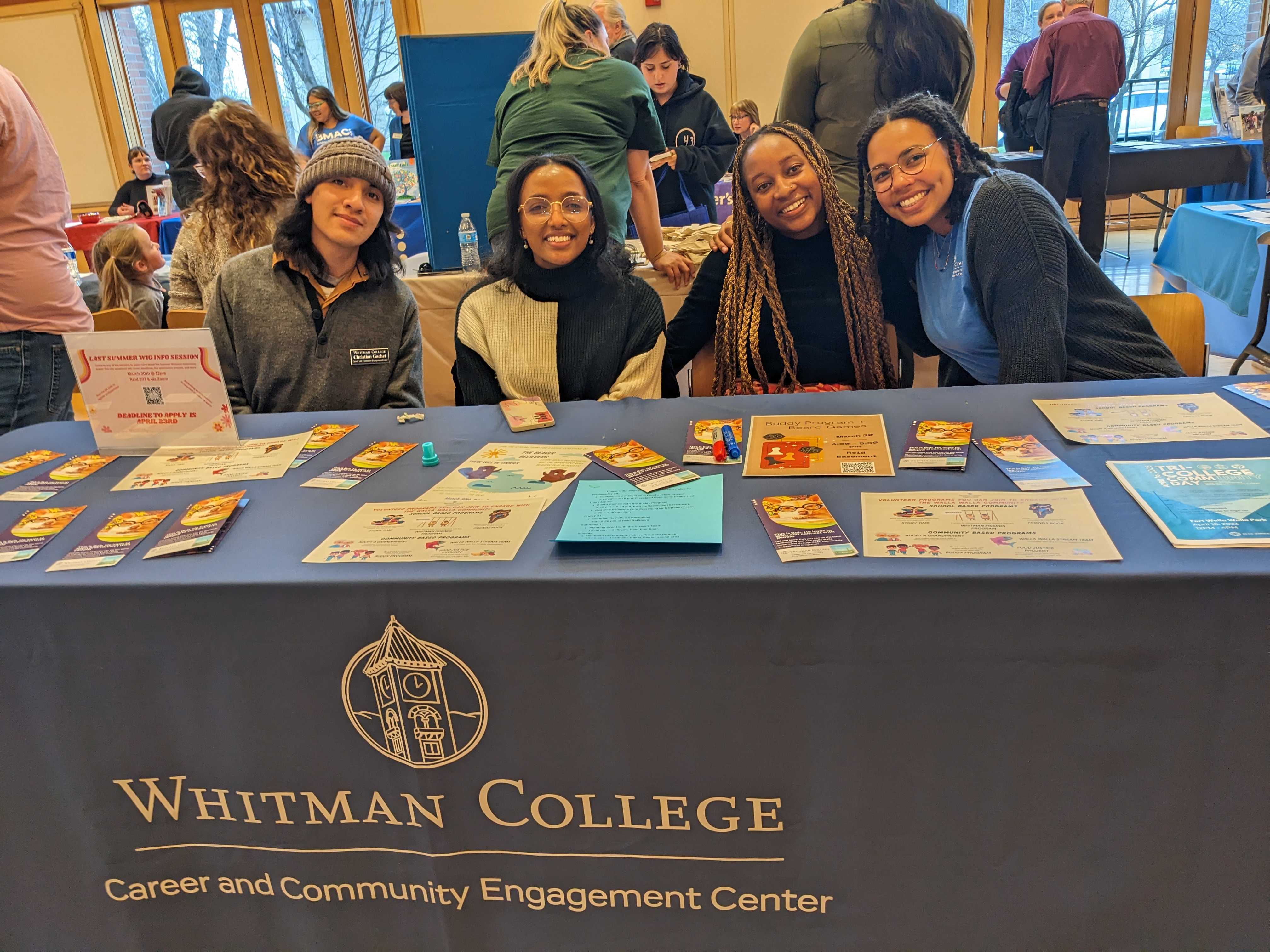 Student volunteers sitting behind a table with a table cloth on top that says Whitman College Career and Community Engagement Center