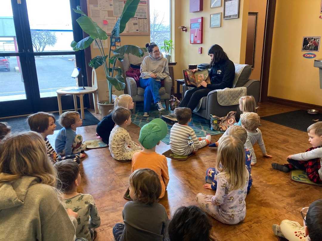 A student volunteer reads to a group of a dozen preschoolers in their pajamas for PJ day