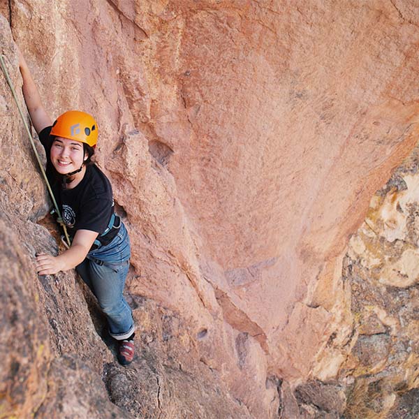 A rock climber smiling, high up on a sheer rock wall.