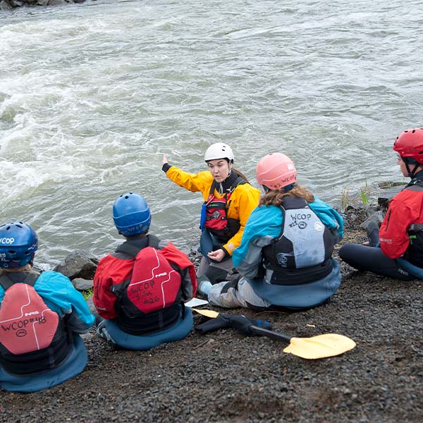 A kayak instructor speaking to students on the edge of the river.