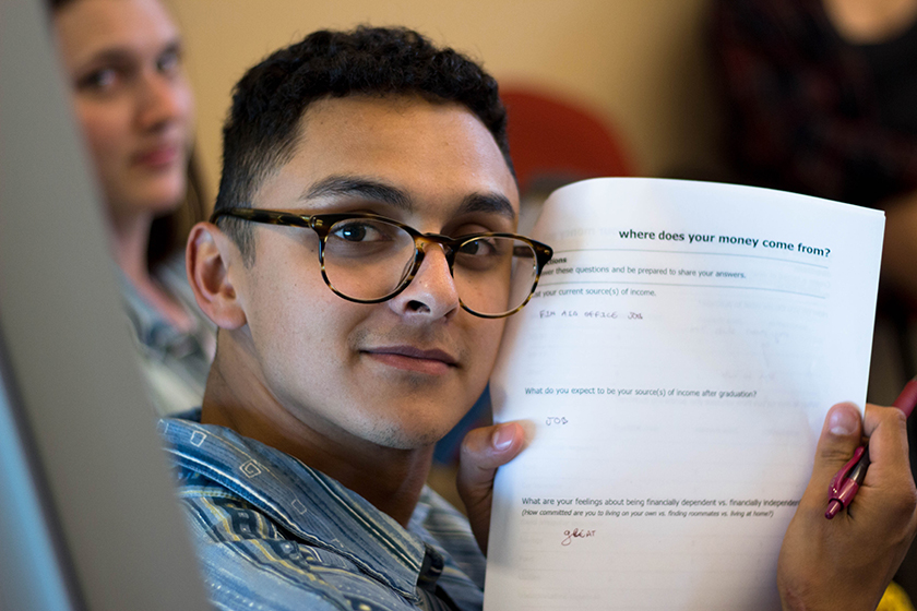 Ricardo Vivanco '18 holds up a worksheet that says "where does your money come from" at a financial literacy workshop.