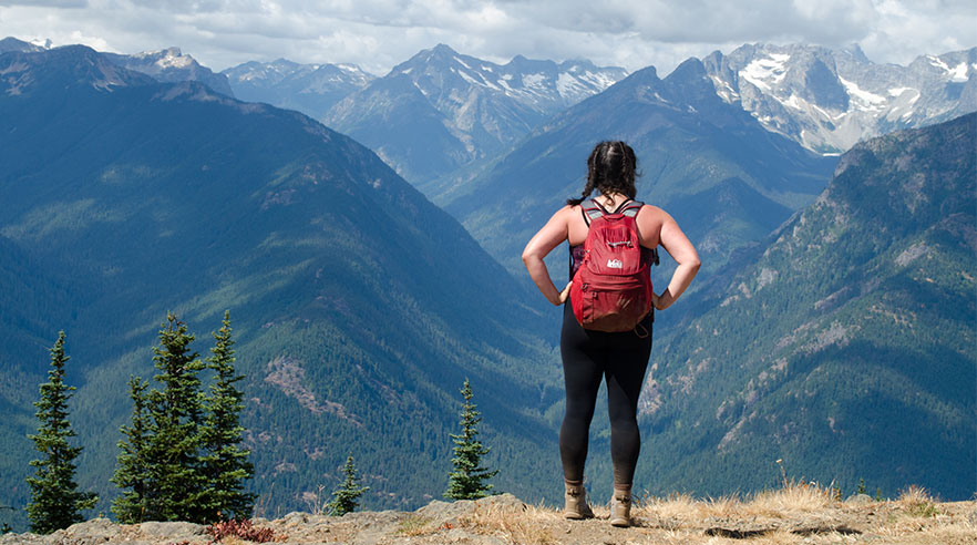 A backpacker observing a view of a snow capped mountain range.