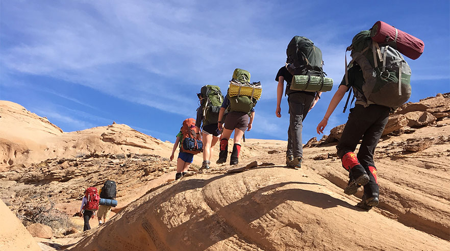 A group of student hikers in a line over large rocks.