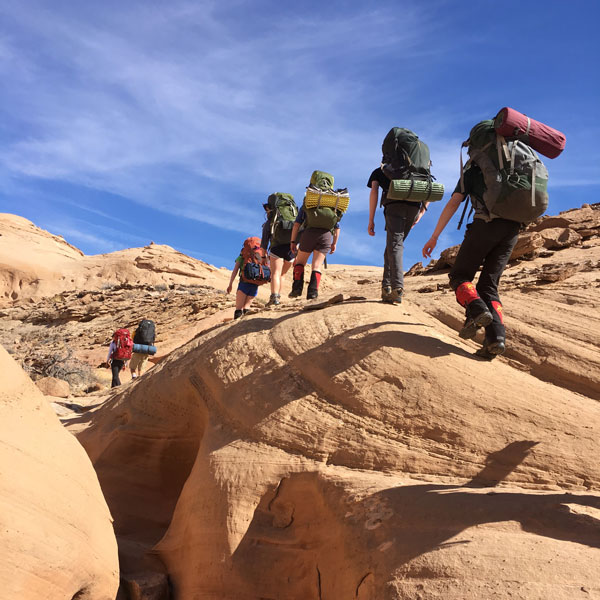 A group of student hikers in a line over large rocks.