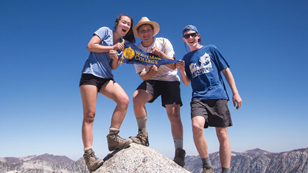 Three students standing on a mountain summit.
