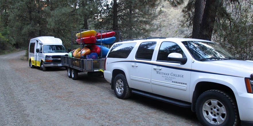 Whitman suburban tows a trailer with kayaks and a Whitman van follows.