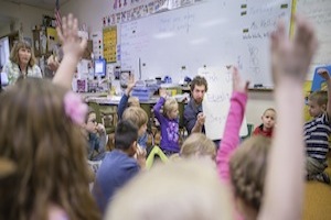 Students raise their hands in first grade classroom