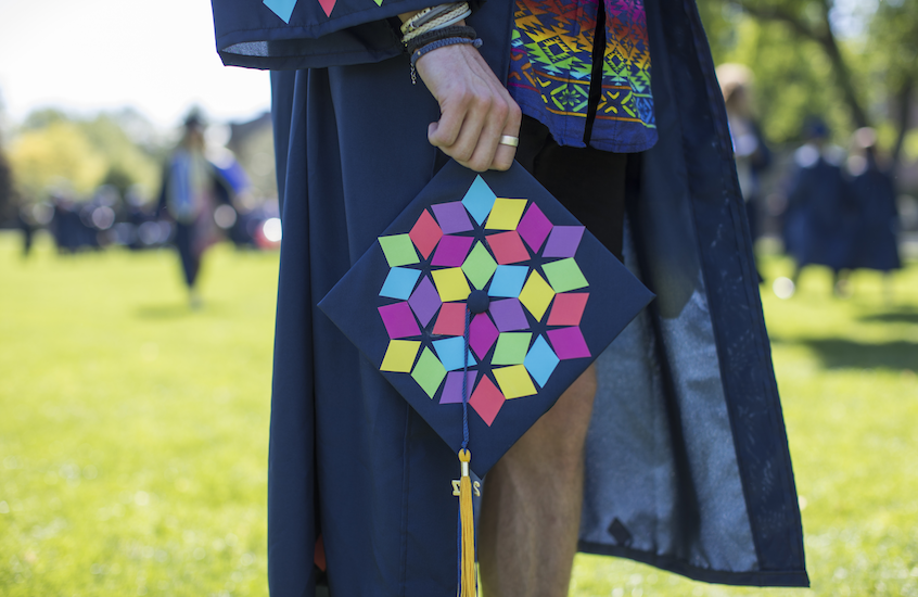 Zach Hartzell holding Commencement cap with colorful cutouts in different shapes