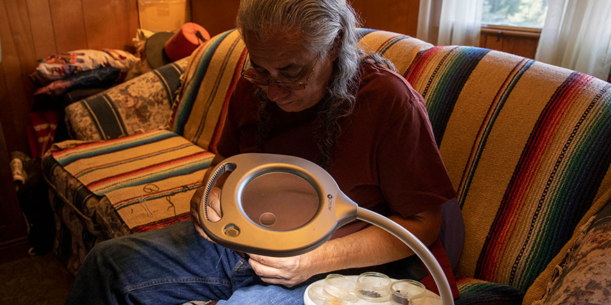 Marcus Amerman works on beading on his couch at his home.