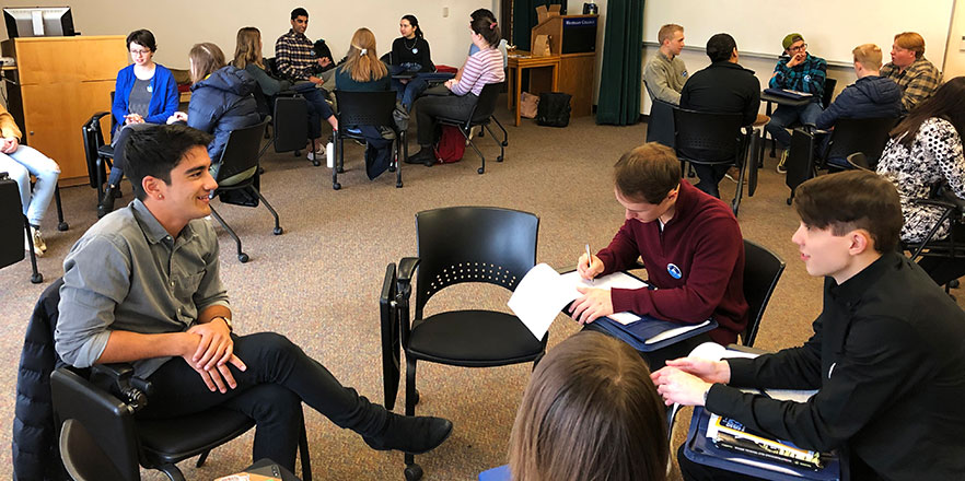 Students sit in chairs and talk to alumni.