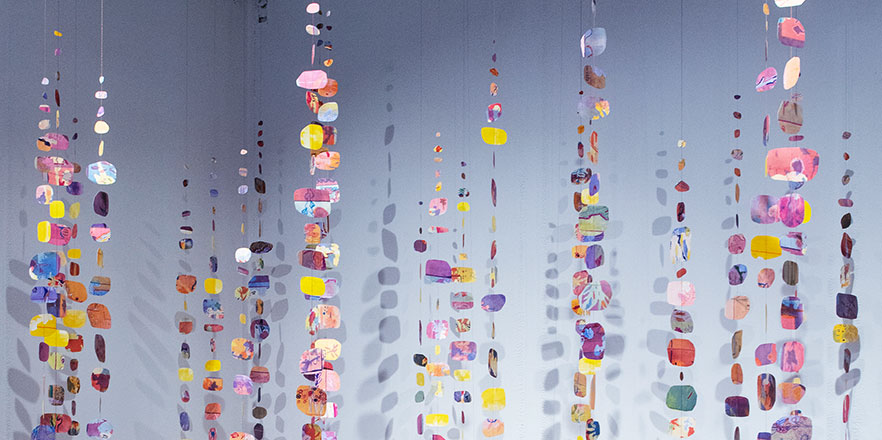 art piece with colorful paper strung on strings hanging from the ceiling 