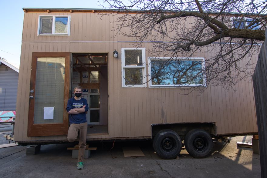 Brayden Preskenis stands in front of a tiny house built on a trailer