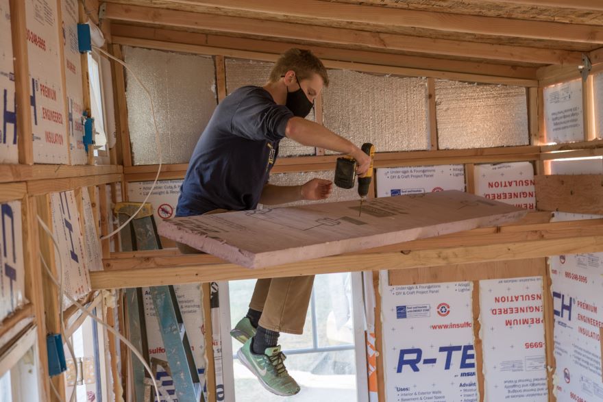 Preskenis sits atop a rafter inside the tiny house and uses a power drill