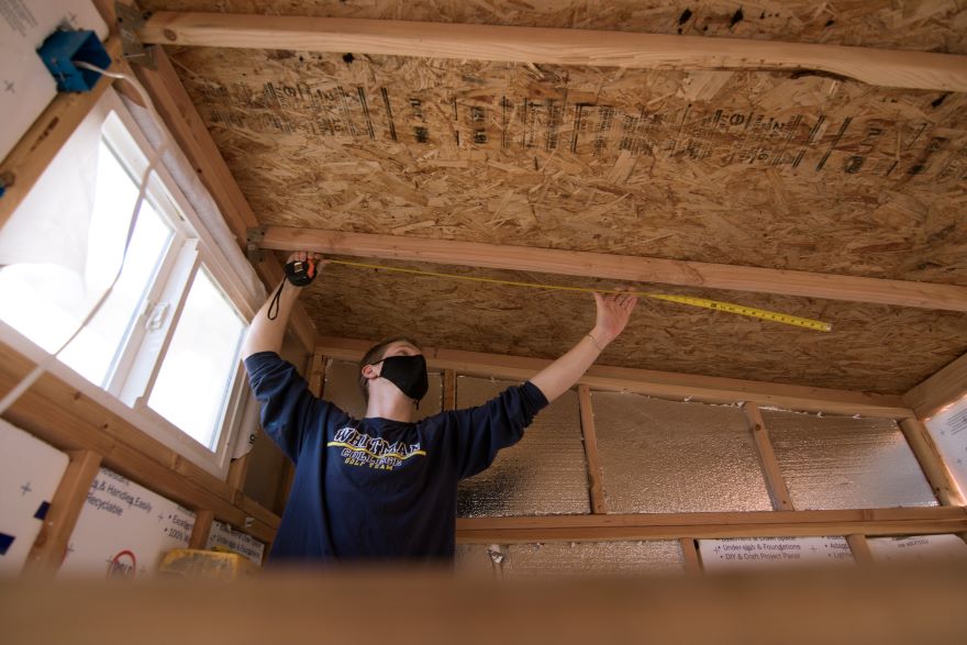 Preskenis reaches toward the ceiling of the tiny house as he measures with a tape measure