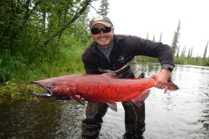 Alum Tyler Dann holds a large salmon in an Alaskan river