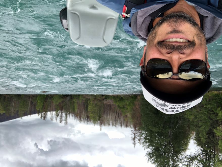 "selfie" picture of Dann driving a boat on a river in Alaska