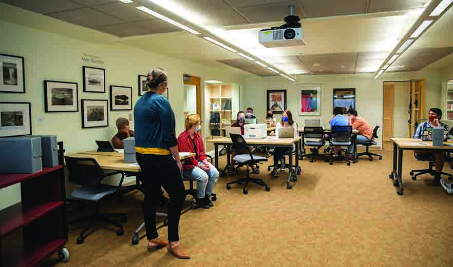 photo of the new Edwards Classroom in Whitman College's Penrose library. Several students are seated at desks facing the camera. A professor stands at the head of the classroom with her back to the camera.