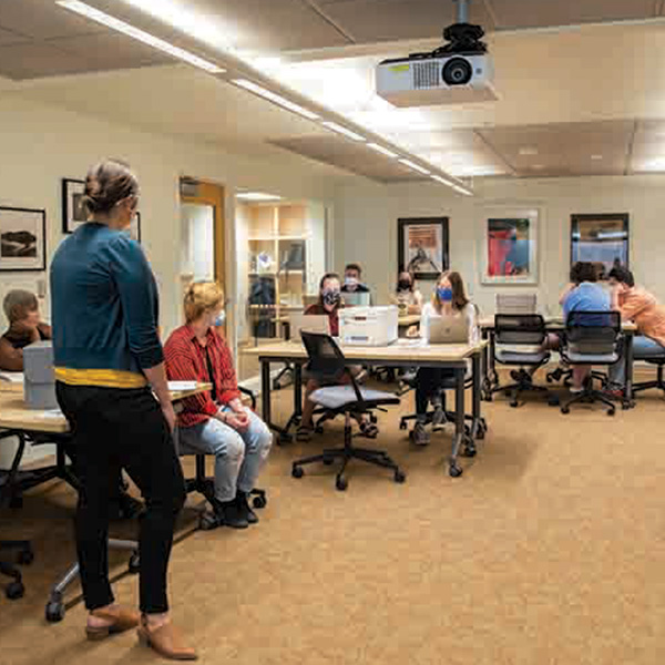 Photo of the new Edwards Classroom in Whitman College's Penrose library. Several students are seated at desks facing the camera. A professor stands at the head of the classroom with her back to the camera.