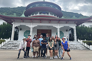 A group photo in front of a white building with red and green roof and marble steps and columns.