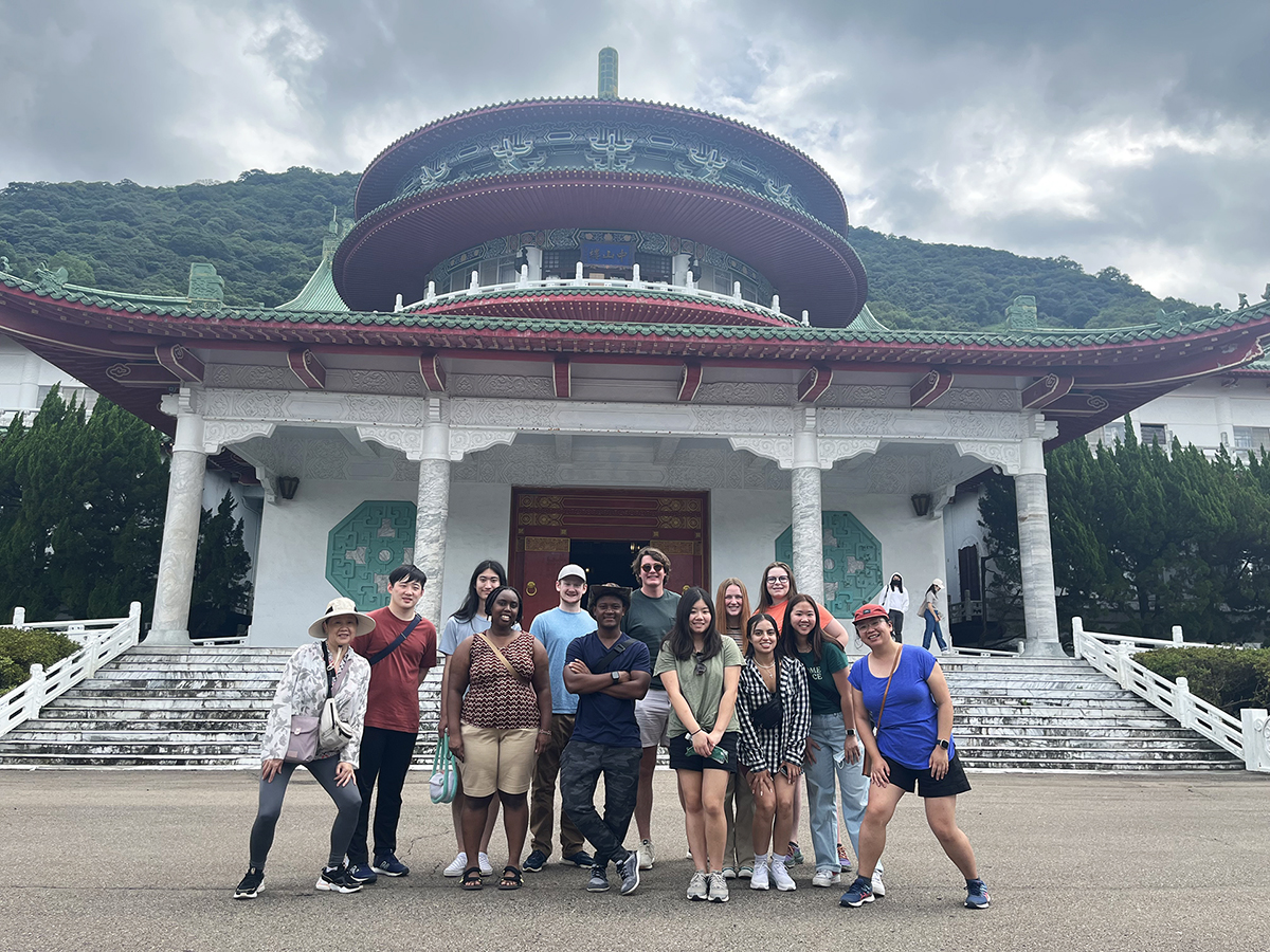 A group photo in front of a white building with red and green roof and marble steps and columns.