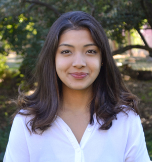 Nishtha Rajbhandari, with long, dark brown hair and wearing a white top, with trees in the background.