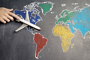 A hand touches a toy airplane on top of a chalk map of the world.