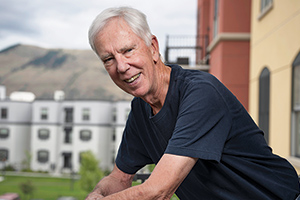 Darrell Baggs stands smiling on a balcony with multi-story apartment buildings in the background